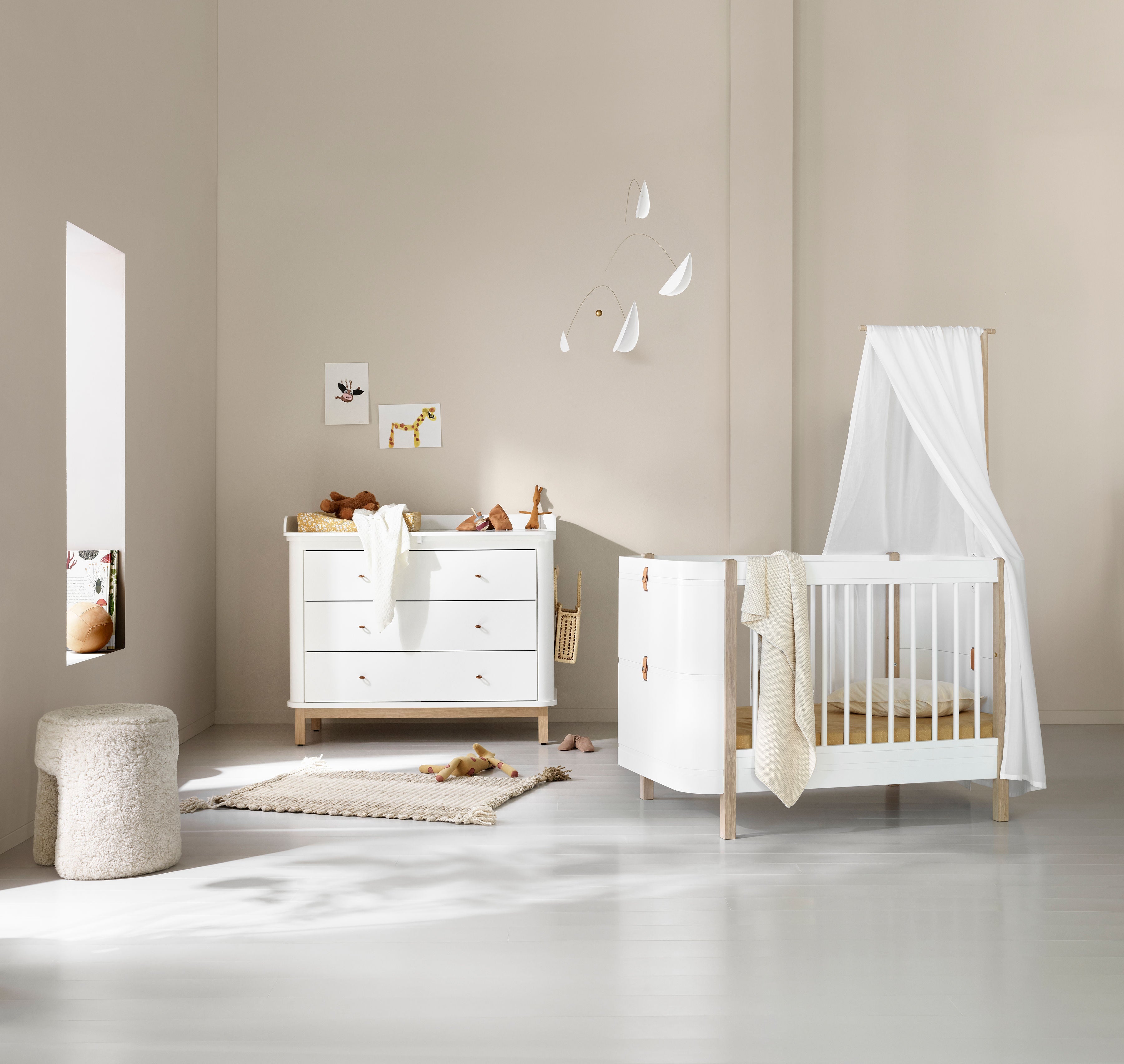 Oliver Furniture Wood værelse med skuffekommode og hvid tremmeseng med sengerand.