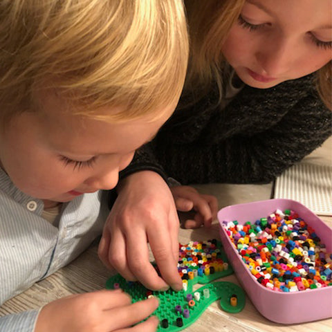 To børn laver perleplader med Hama perler på en grøn plade